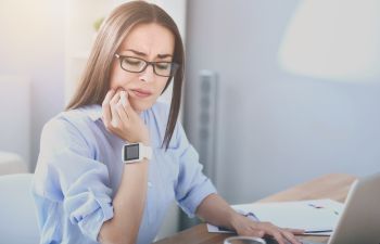 A concerned woman with dental pain working at a desk with a laptop.