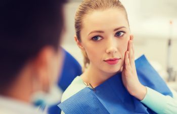 A woman with toothache sitting in a dental chair and explaining the issue to the dentist.