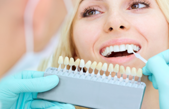Dentist matching porcelain veneer color to woman's teeth color.