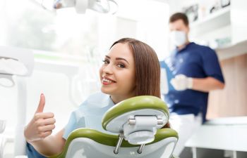 A woman giving a thumbs up while sitting in a dental chair.
