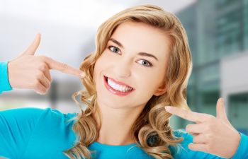 A smiling woman pointing at her white teeth