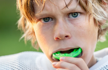 A young boy with a green mouth guard in his mouth.