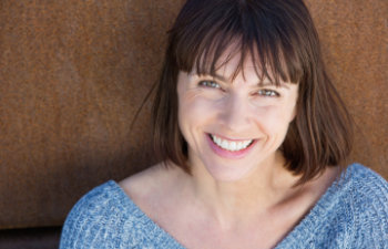 A woman smiles while leaning against a rusty wall.