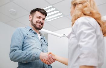 A man and a woman shaking hands in a dentist's office.