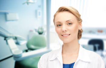 A female dentist standing in front of a dental chair.