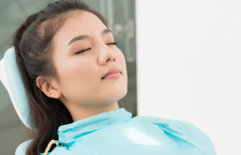 A woman sitting in a dental chair with her eyes closed.