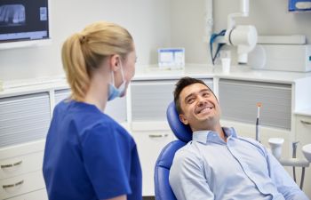 A man sits in a dental chair smiling at a dental professional who is standing beside him in a dental clinic.