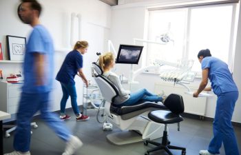 A woman sitting in a dental chair next to a screen with a dental imaging and dental team preparing for the treatment